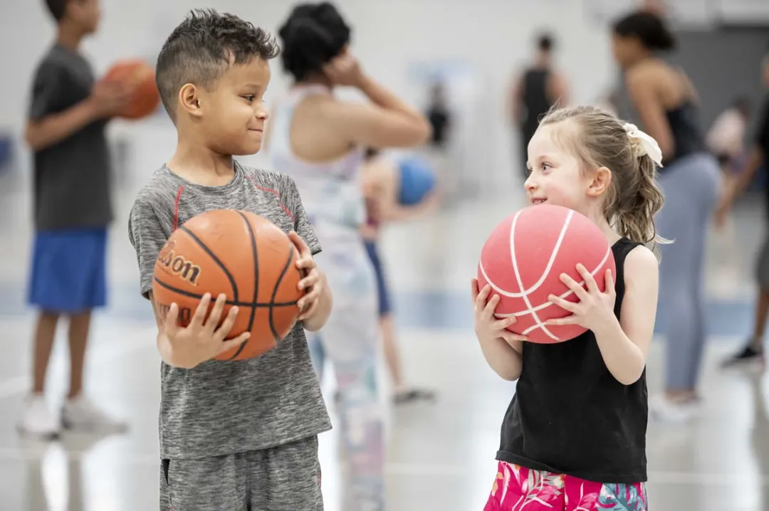 A young girl and boy play with basketballs.