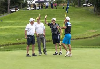 Four golfers on a golf course, two of them are high fiving