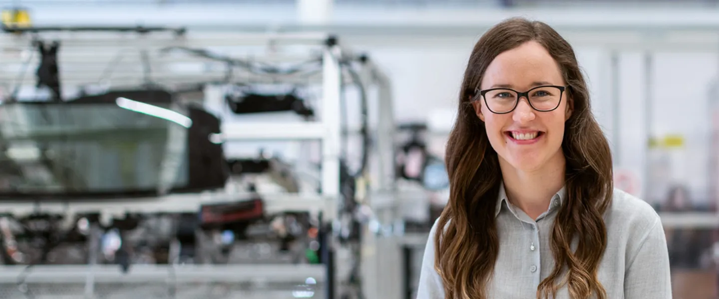 A smiling woman stands in a factory.