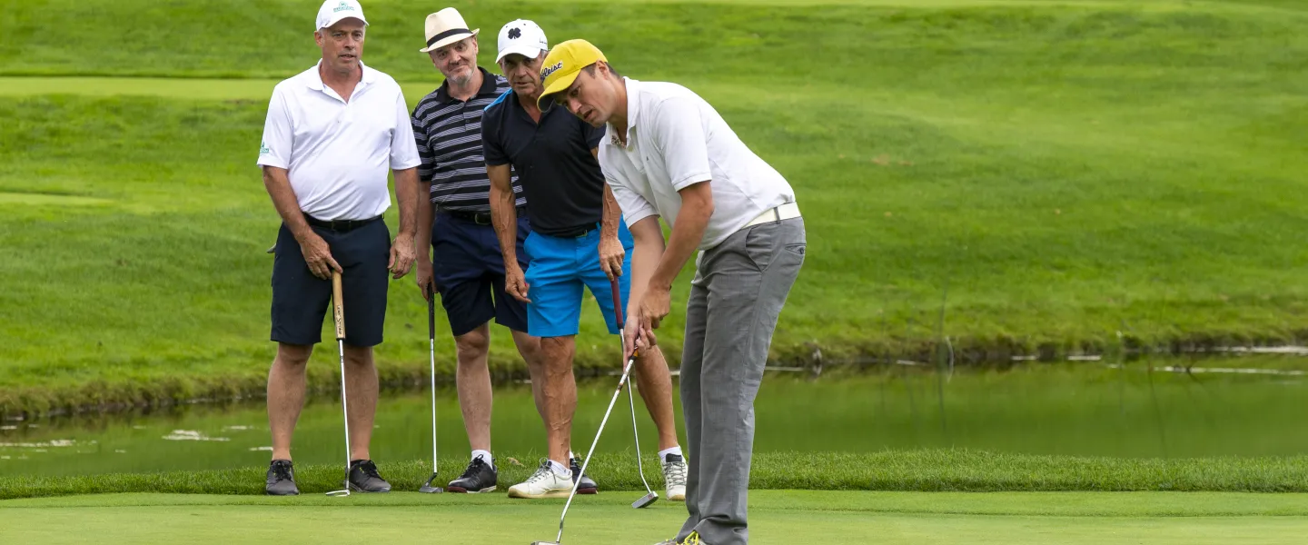 A golfer about to swing, and three others watching on a golf course