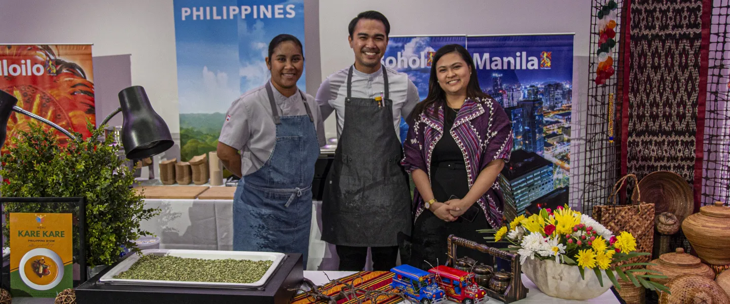 Three chefs standing at a Philippines table covered in food and cultural objects.