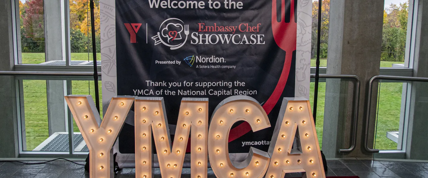 A banner that reads "Welcome to the Y Embassy Chef Showcase". In front is "YMCA" spelled in large light-up letters.