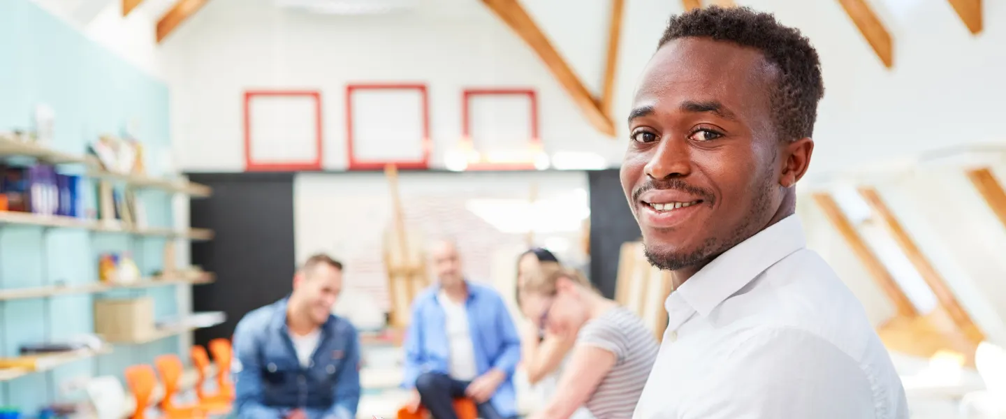 Man sits in room with other people, smiling.