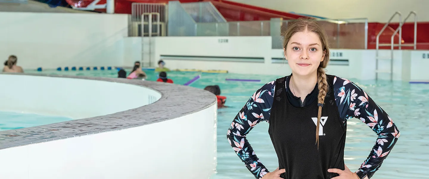 A swimming instructor kneels in the shallow end of the pool.