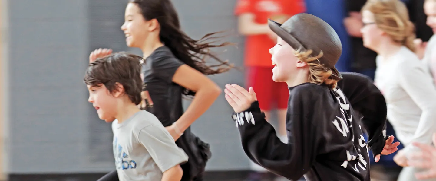 A group of children run in a gymnasium.