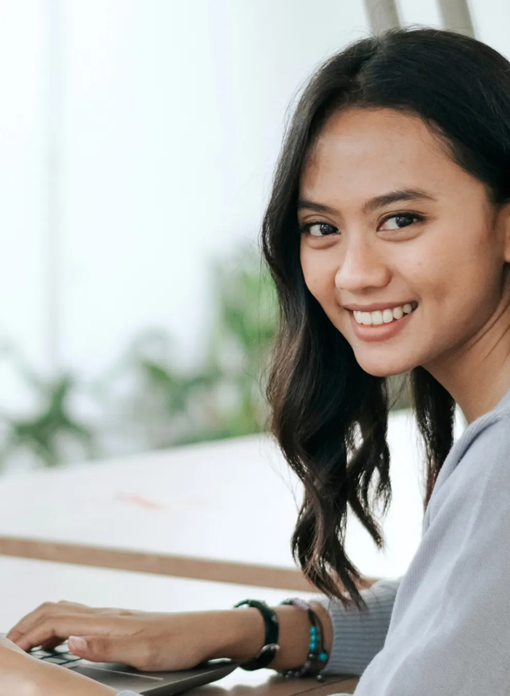 A young Asian woman smiles while working on her laptop.