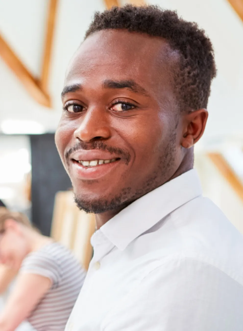 Man sits in room with other people, smiling.