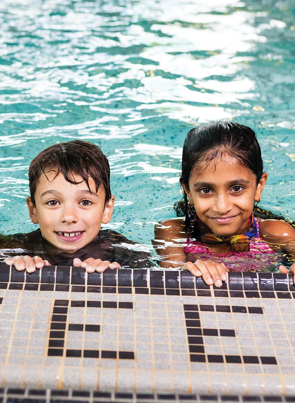 Three children at the edge of a swimming pool.