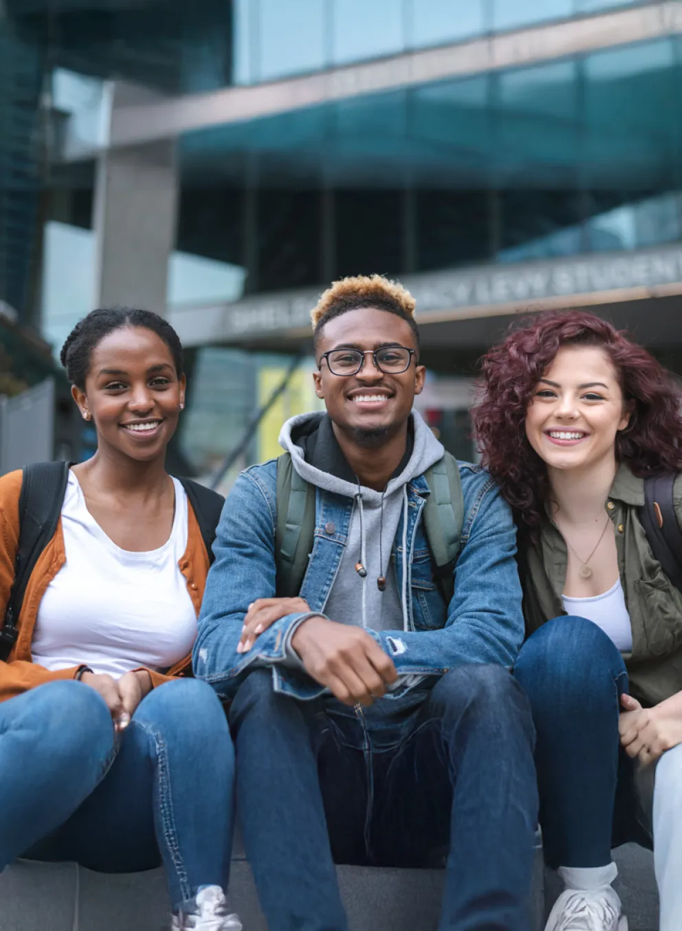 Three diverse youth sit on steps.