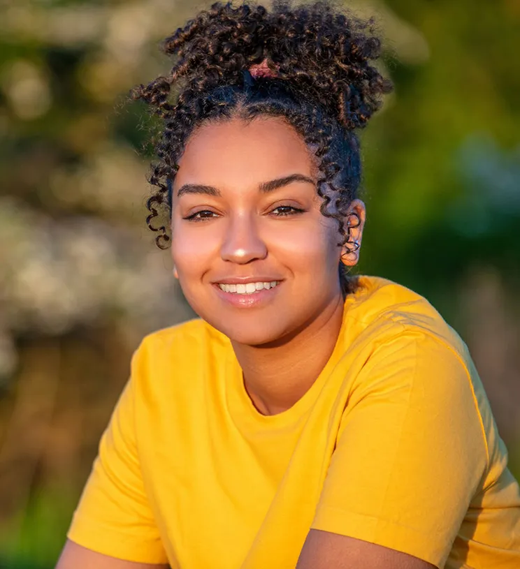 A teenage girl wearing a yellow t-shirt looks into the camera.