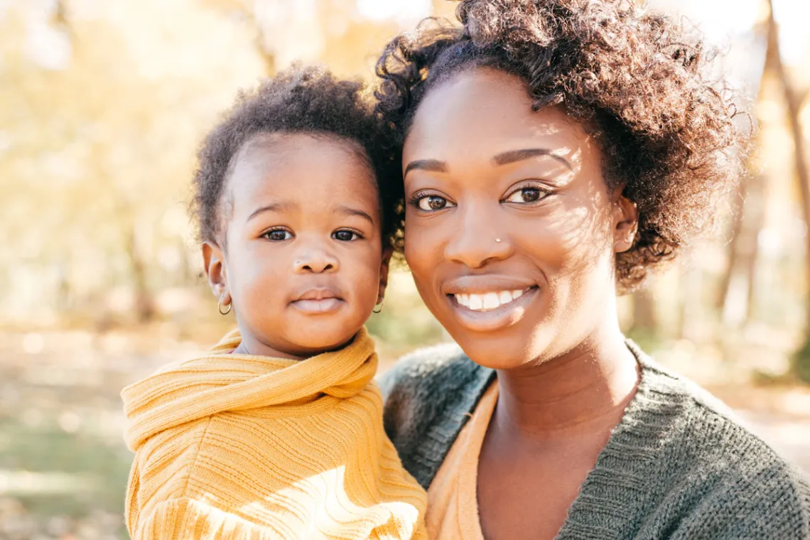 A smiling Black woman holds her young child.