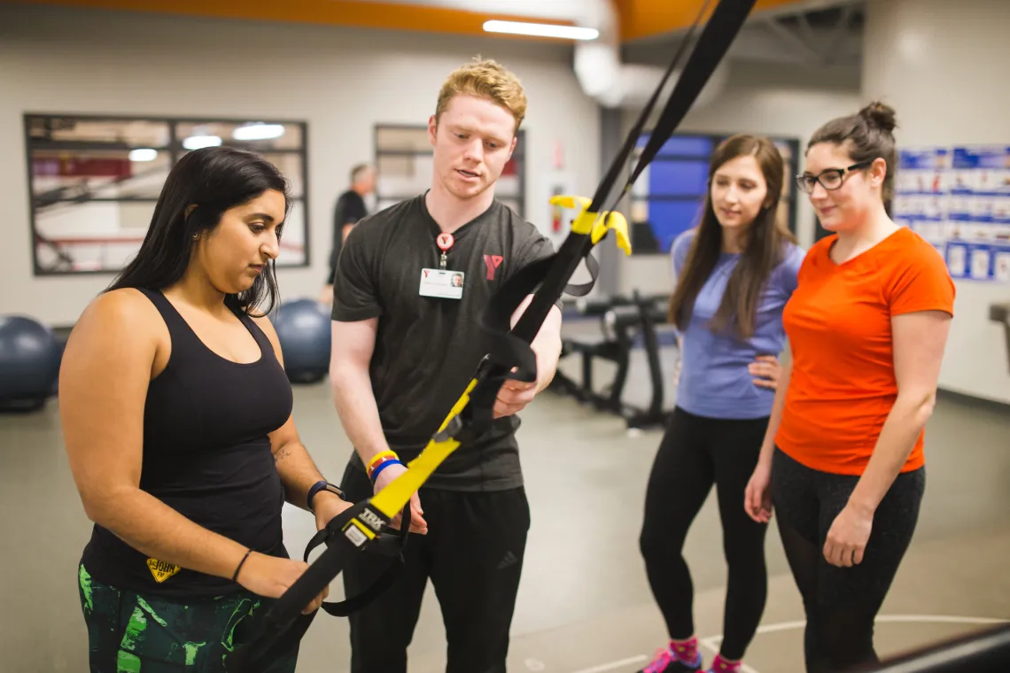 A personal trainer helping a client at a workout machine as two others watch