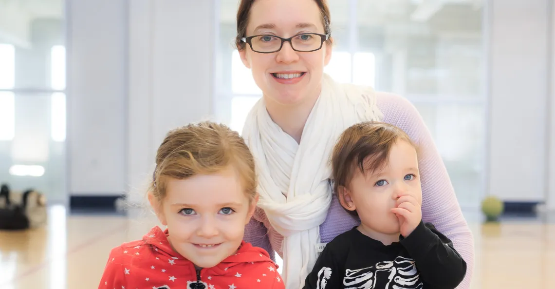 A mother and her two children sit on the gymnasium floor.