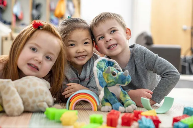 Three kids at daycare smiling at camera.