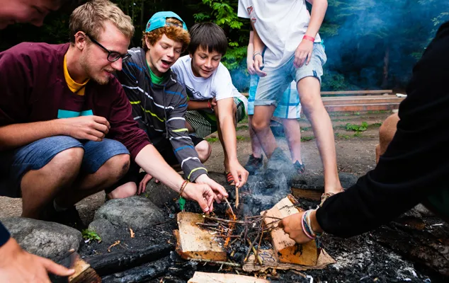 A camp councilor supervises campers who are lighting a camp fire.