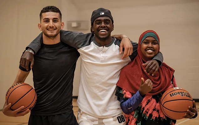 Three young adults playing basketball in the gymnasium.